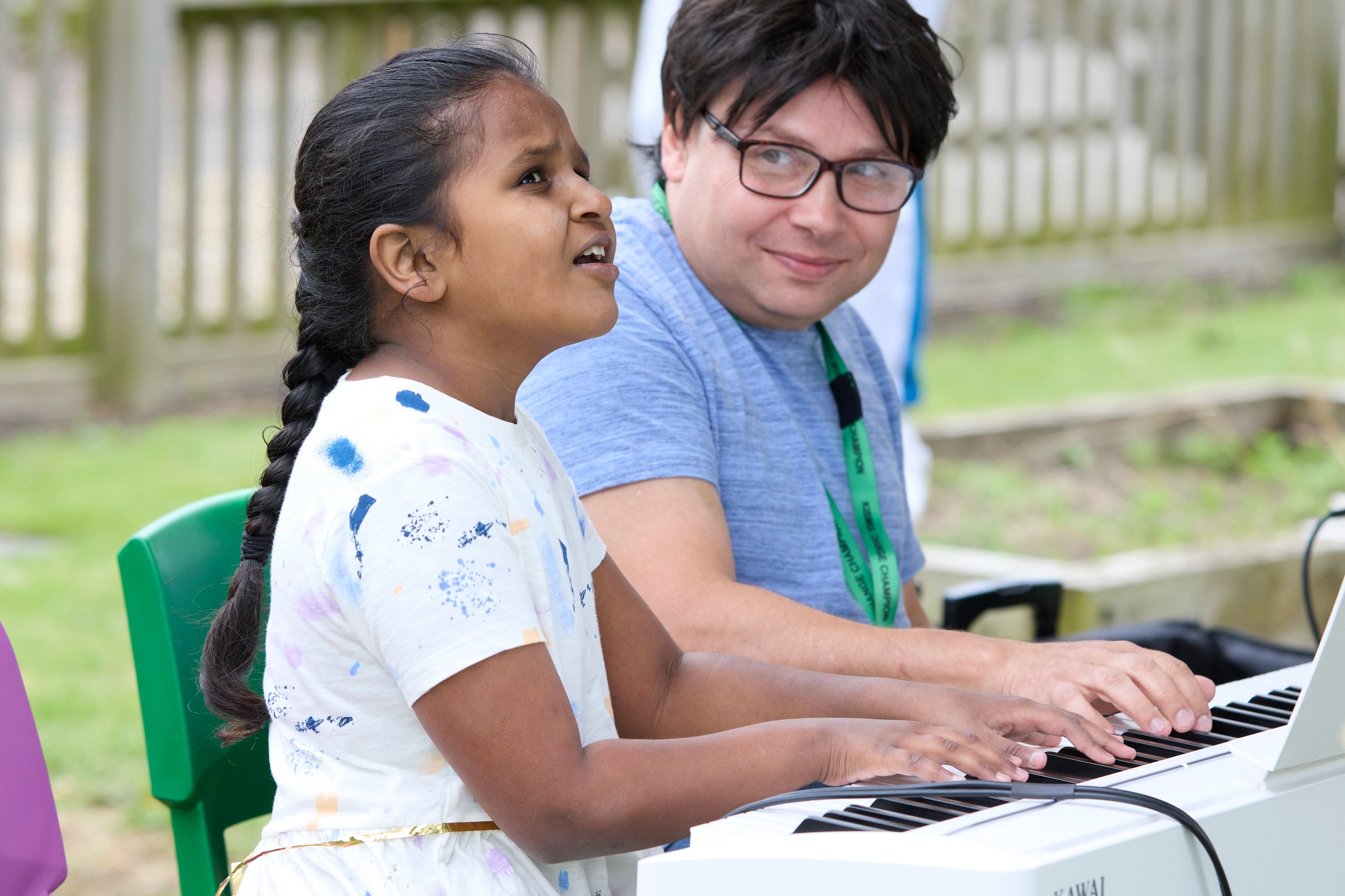 A girl singing while playing the piano with a man.