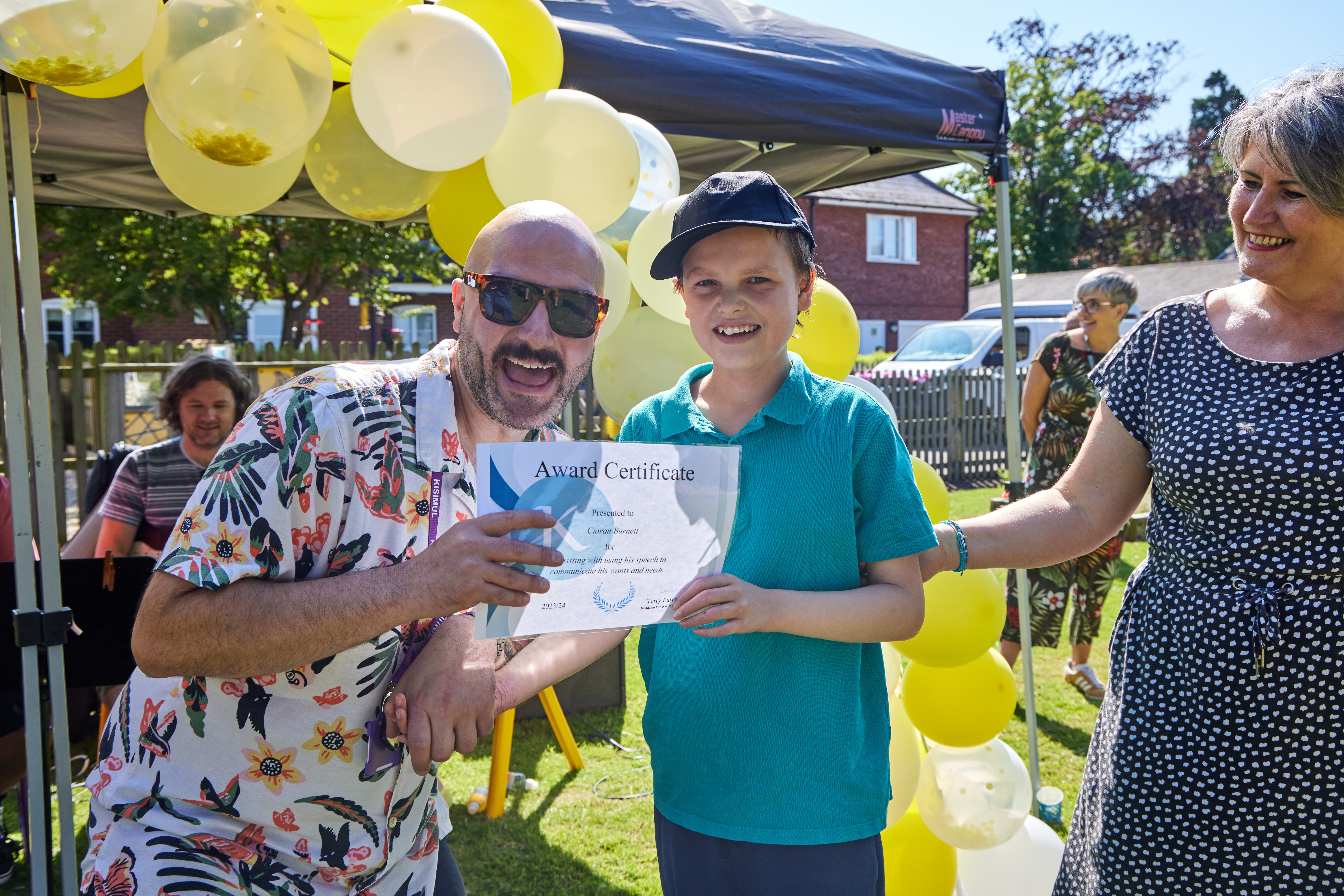 Man and boy holding award certificate, balloons in background.